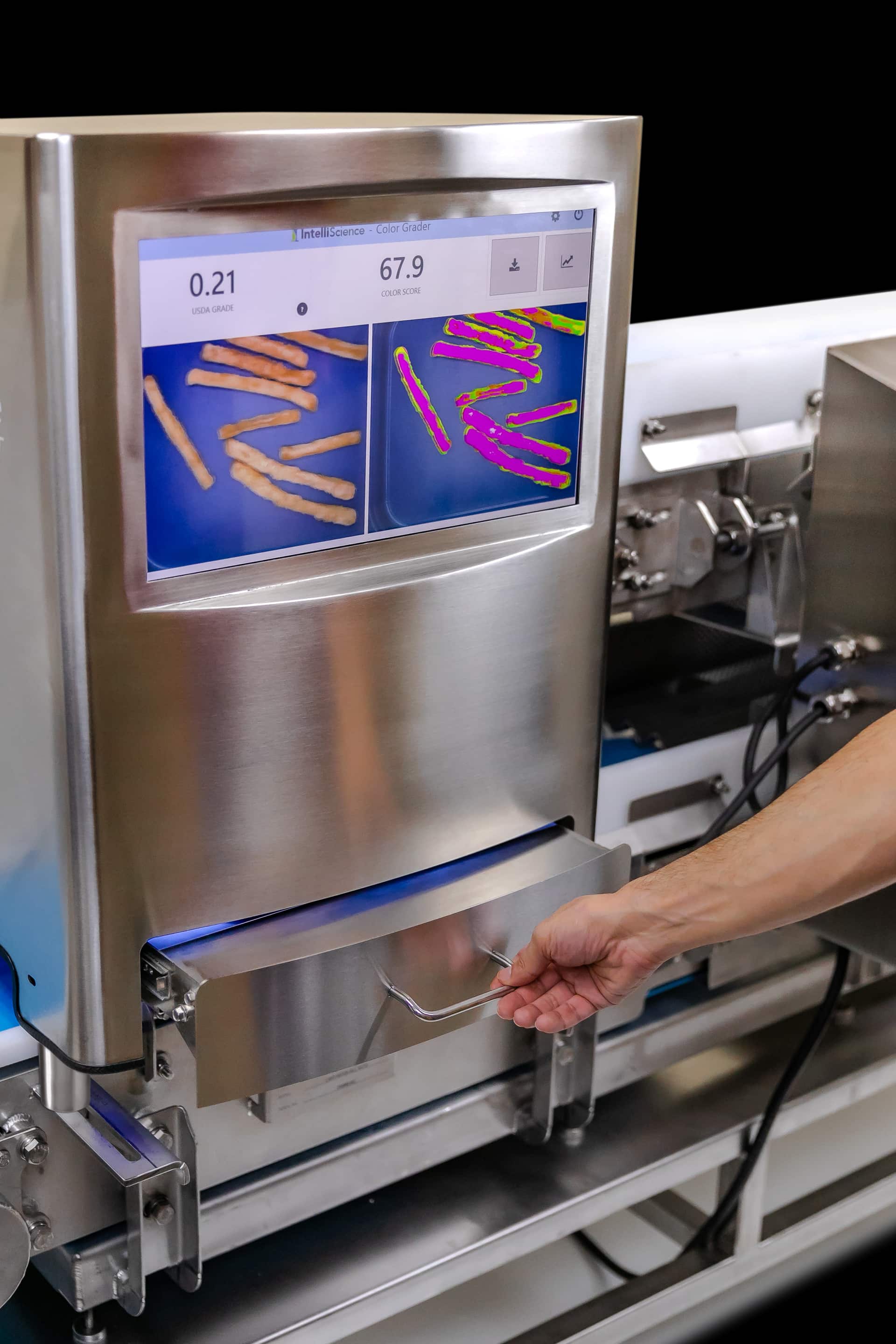 The iVIA screen showing a raw sample on the left and detected defects highlighted on the right, with a hand resting on the sample tray.